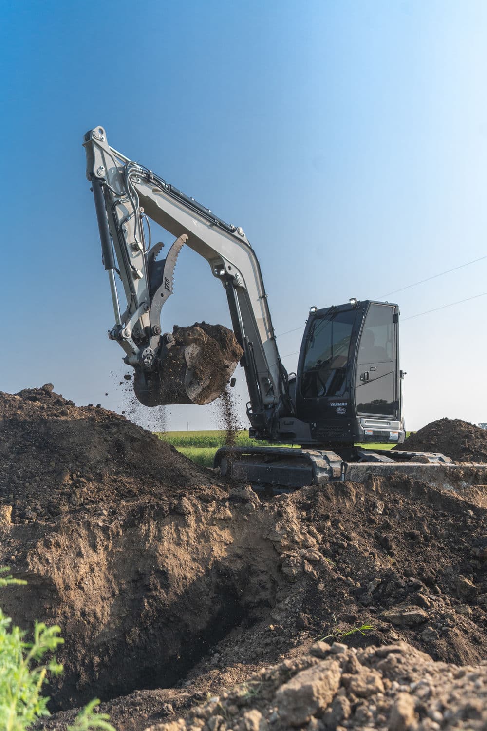 Excavator digging soil on a construction site under a clear blue sky.